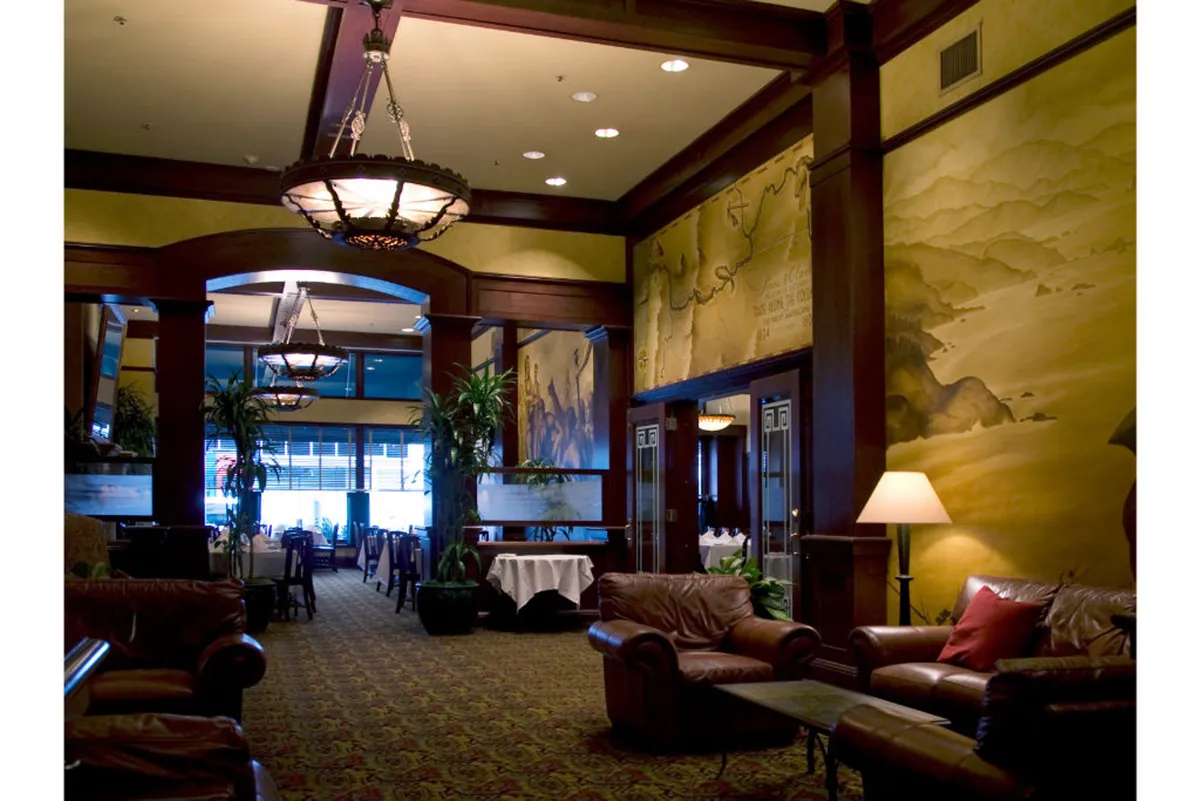 An elegant yet cozy dining and social area with leather sofas, a decorative wall mural, eye-catching chandeliers, and a variety of potted plants. The space is designed for gatherings, relaxation, and offers a sophisticated yet approachable vibe.