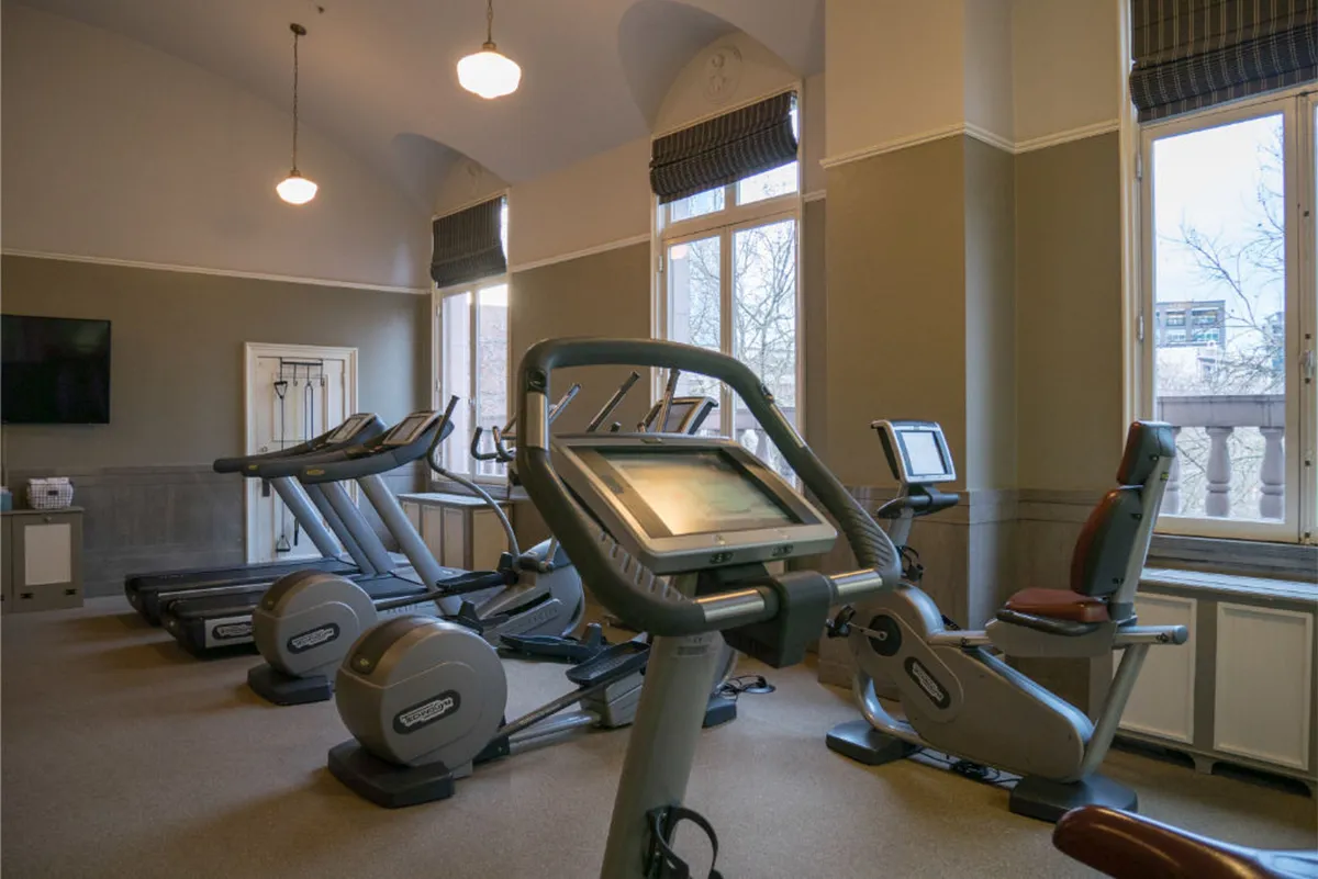 A modern fitness center showcasing treadmills and elliptical machines positioned near large windows, with ample natural light and a wall-mounted TV, creating an inviting space for guests to focus on wellness and exercise routines.
