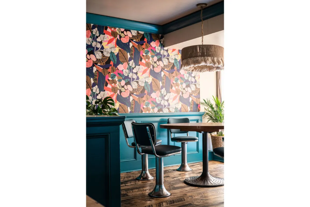 A cheerful and relaxed dining space adorned with colorful floral wallpaper, stylish cushioned seating, and a unique, sculptural light fixture. The playful art-inspired decor invites socializing and creative conversation.
