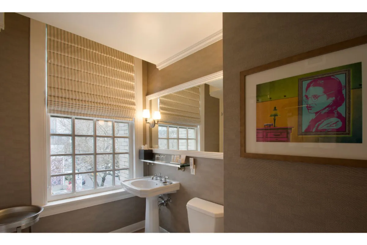 A bright, contemporary bathroom scene with a sink and mirror, striking artwork on the wall, and morning sunlight streaming through a window. The space feels artistic and refreshing, inviting moments of calm while preparing for the day.