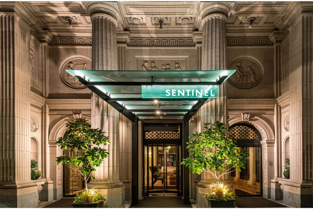 This image features the illuminated 'SENTINEL' sign above a grand entrance framed by ornate columns, with lush green foliage accenting the entryway. Warm lighting enhances the building’s sophisticated facade, inviting guests into the heart of Portland’s West End.