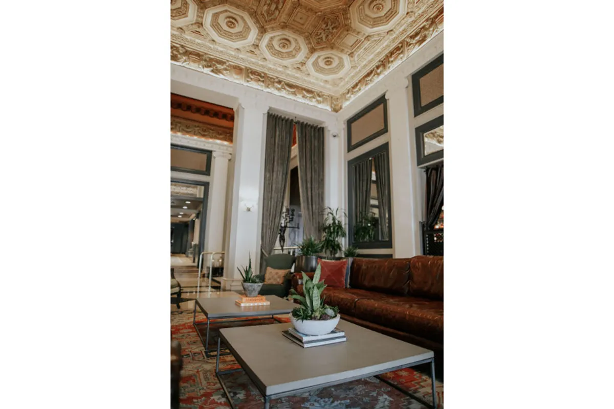A welcoming lounge space with an ornate ceiling, plush comfortable seating, decorative plants, and modern coffee tables. The scene is set for relaxation, intimate conversations, and quiet moments, enhanced by sophisticated décor and natural accents.