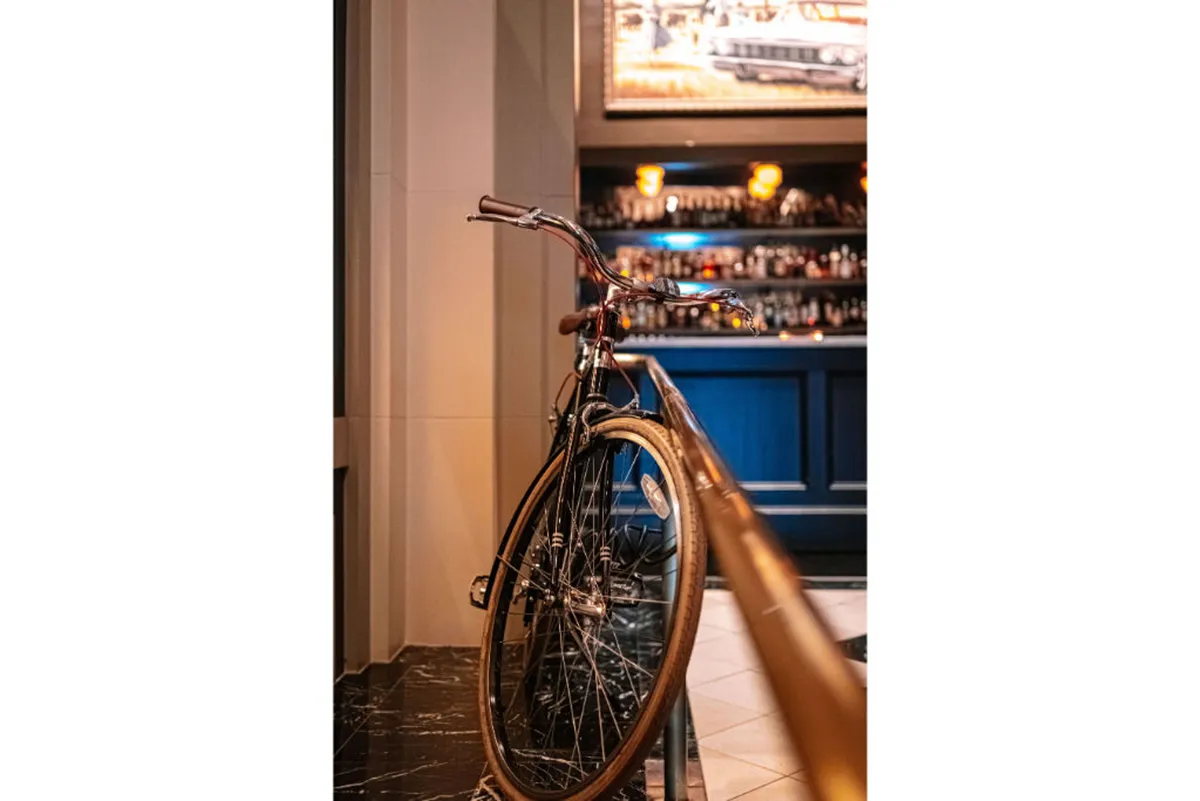 A stylish lounge area featuring a bicycle as a decor highlight, a chic bar, and wall art. The environment is contemporary and relaxed, ideal for casual socializing and reflecting the hotel's unique, creative character.