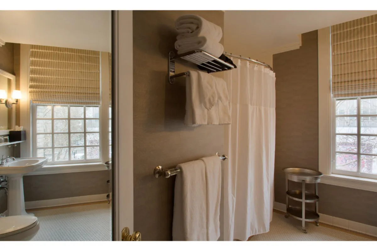 A serene bathroom interior featuring a shower with a curtain, a sink with ample counter space, a large window letting in morning sunlight, and a neatly arranged towel rack. The space exudes calm and relaxation, perfect for self-care rituals.