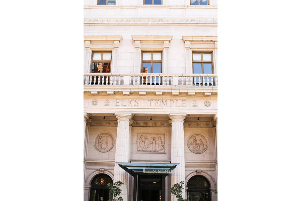 The image highlights the historic 'ELKS TEMPLE' inscription, intricate architectural flourishes, and a glass canopy over the entrance. The facade exudes elegance and historic charm, hinting at Portland's rich cultural backdrop.