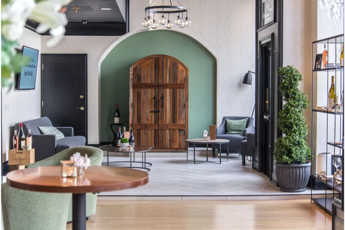 An inviting indoor lounge area with plush seating, a green accent wall, and a shelf lined with bottles. The atmosphere is intimate and relaxed, suited for casual meetings, wine tastings, or winding down after a day out. The space encourages socialization and moments of quiet reflection.